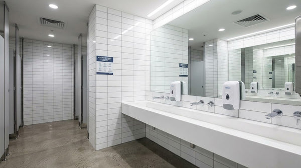Commercial wall-mounted foam hand soap dispensers in a modern Australian workplace washroom with chrome fixtures